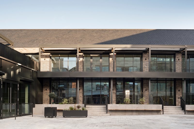 Two-story glazed facade with metal railings and planted boxes opening onto a paved courtyard