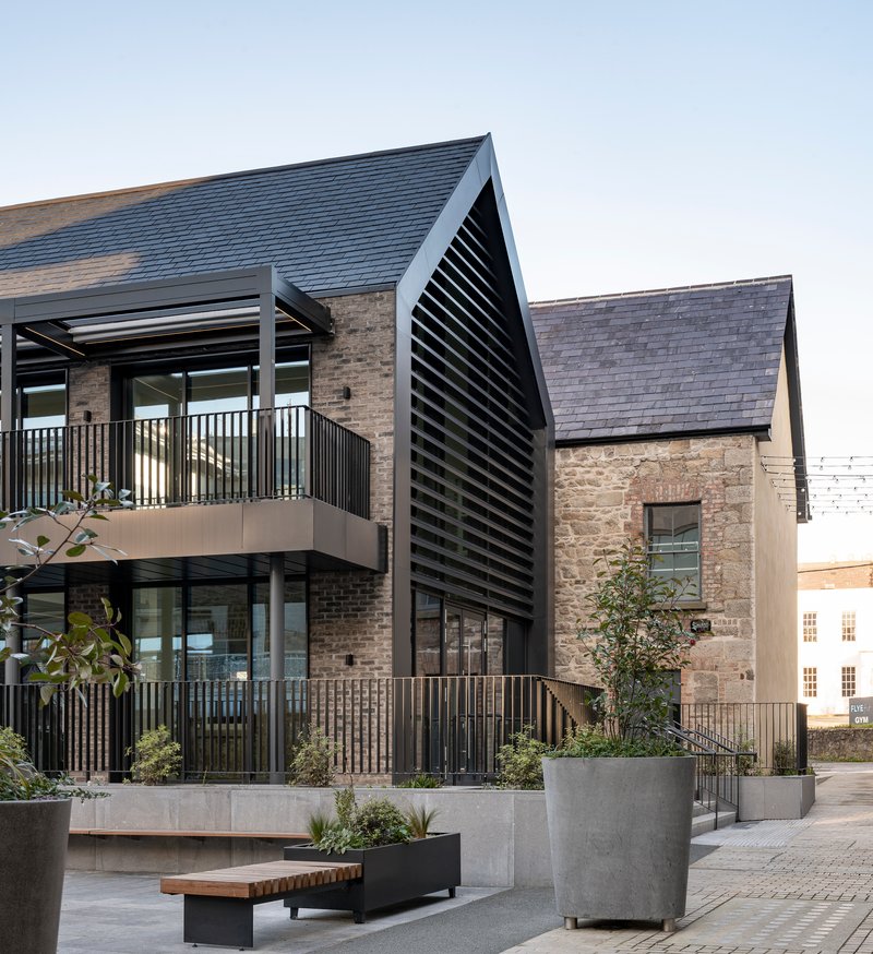 Gabled volume with black louvered screen adjacent to stone masonry and planted concrete planters
