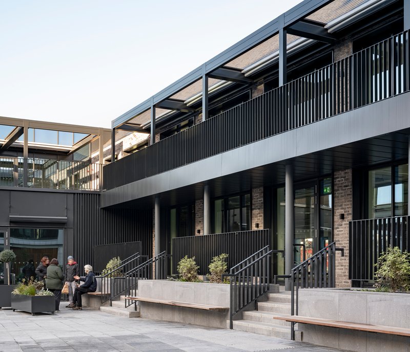 Raised concrete planters with metal railings and benches beneath a cantilevered walkway with exposed structure