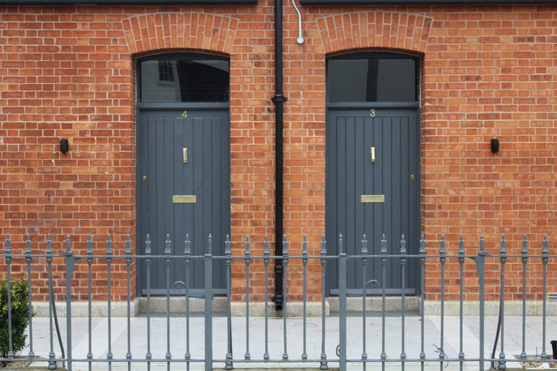 Two grey paneled entrance doors with arched transoms set in red brick facade behind metal railings