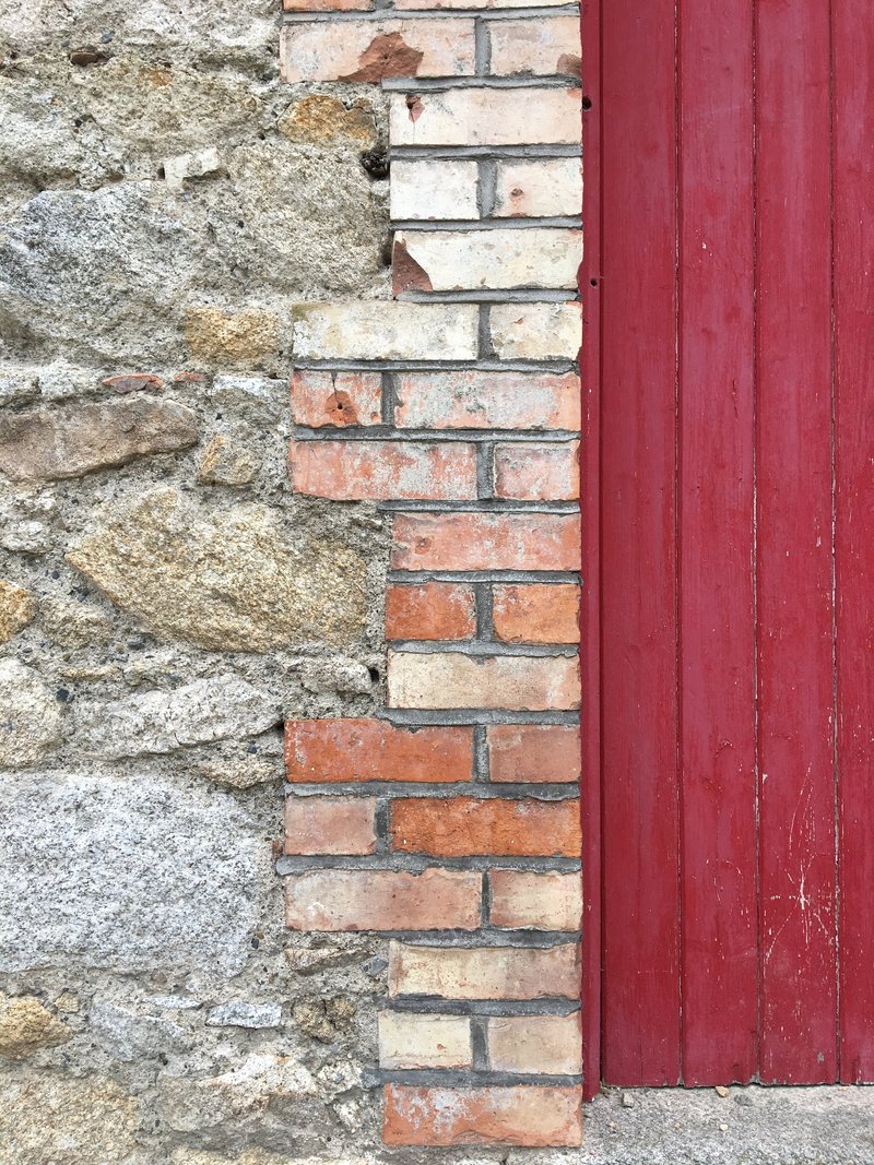 Detail of weathered stone wall meeting salvaged brick infill and painted timber door surround
