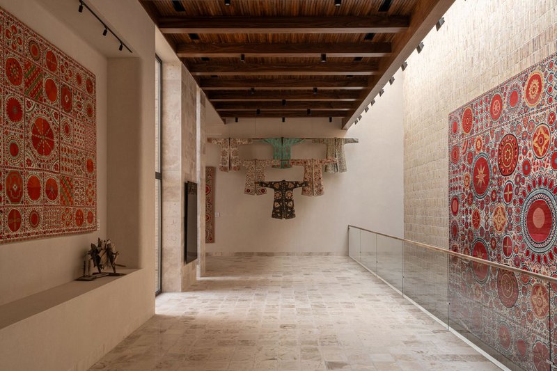 Gallery space with exposed timber ceiling beams and embroidered textile hangings on white walls