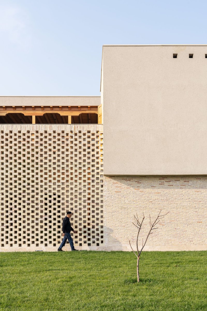 Perforated brick screen wall with a person walking past a young sapling in the lawn