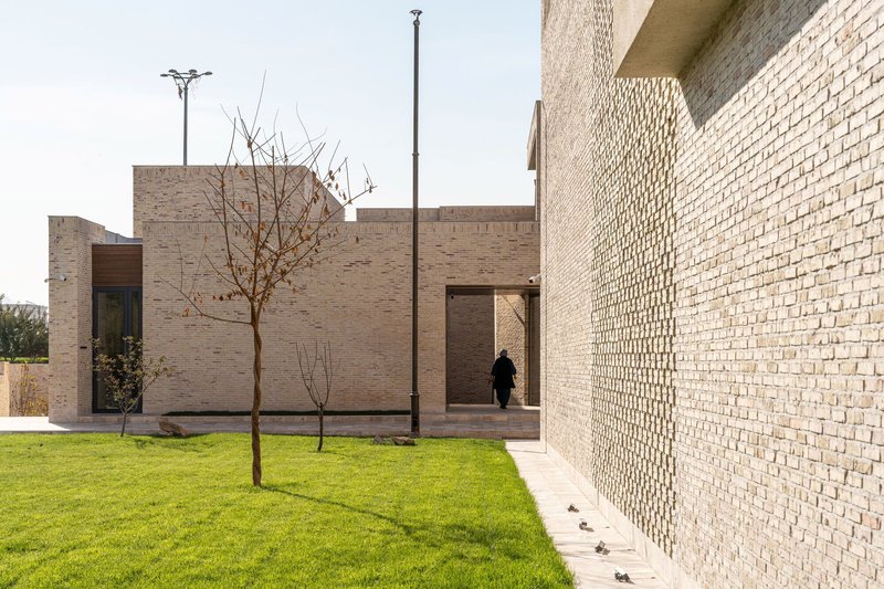 Courtyard with lawn and young trees bordered by perforated brick walls and a figure in the threshold