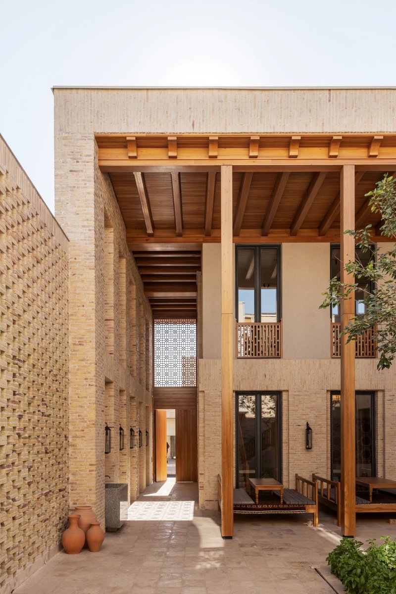Covered courtyard entrance with exposed timber beams and patterned brick walls in afternoon light