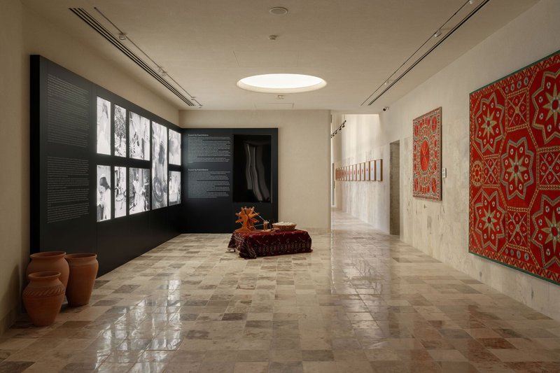 Exhibition hall with backlit photograph wall, ceramic vessels, and textile displays