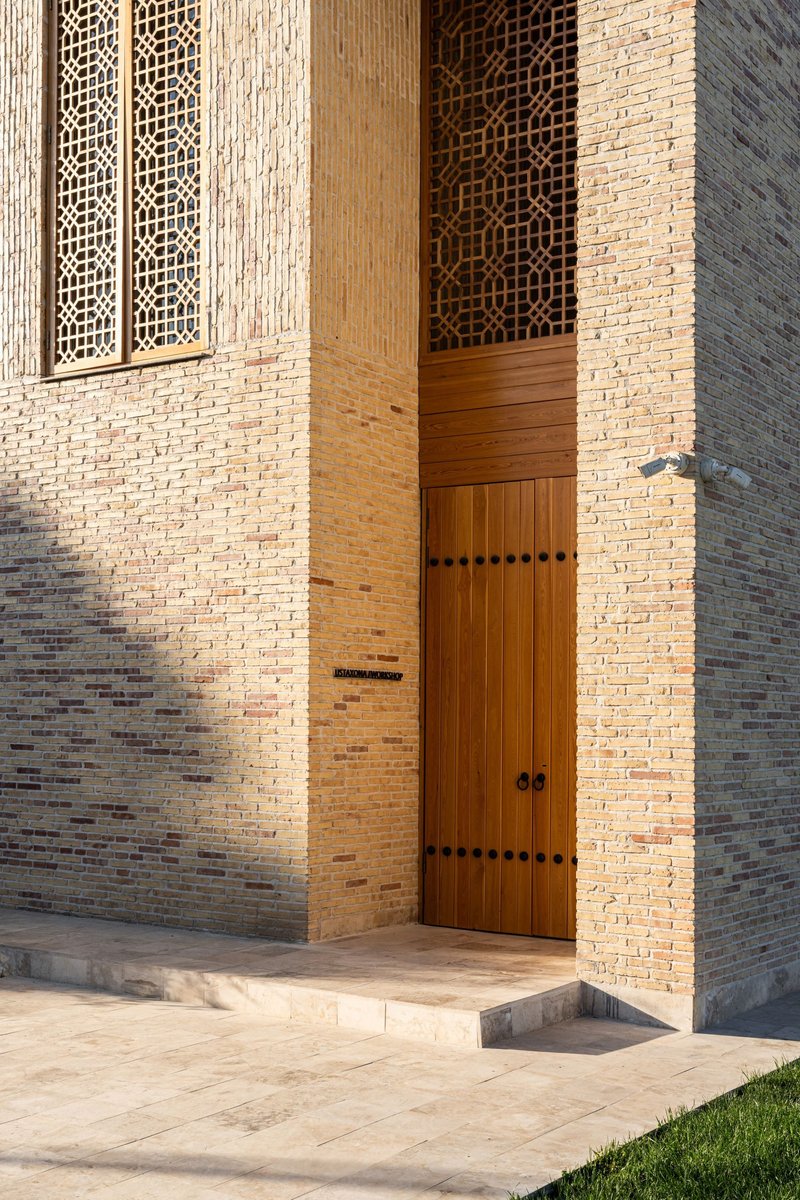 Tall wooden entrance door set within buff brick walls with decorative lattice screens above