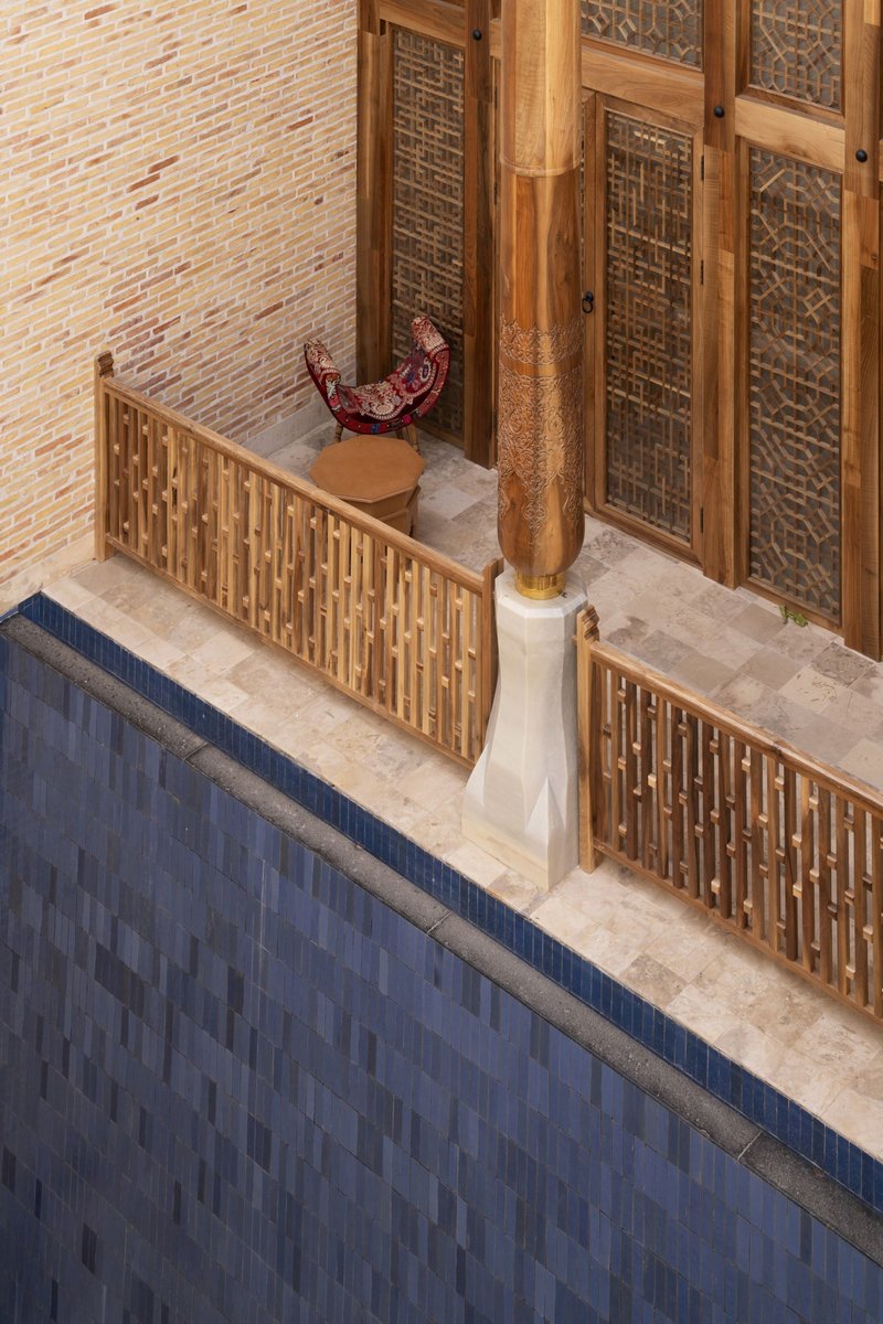 Overhead view of carved timber screens and column base around a tiled reflecting pool at dusk