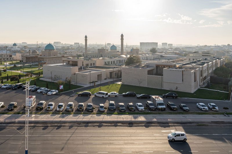 Aerial view of brick building volumes and parking lot with minarets beyond at sunset