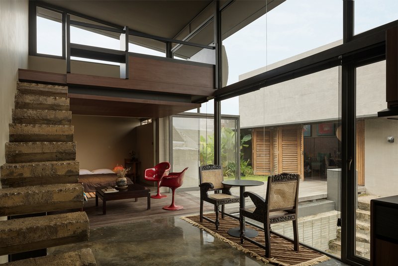 Double-height living space with cantilevered mezzanine and exposed concrete staircase overlooking a planted courtyard