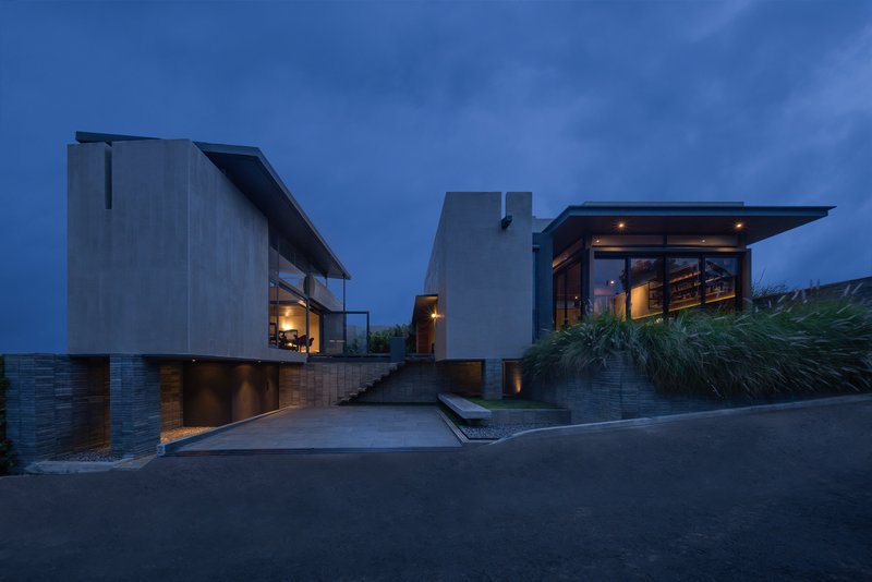 Street view of stacked concrete volumes with timber base and planted grasses at dusk