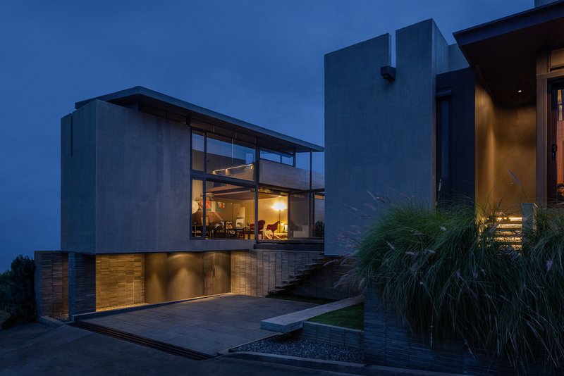 Two-story concrete facade with glazed upper living space and landscaped courtyard at twilight