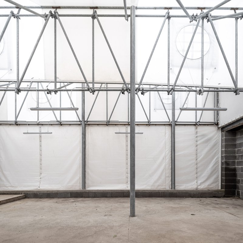 Interior courtyard with galvanized scaffolding frame supporting white tarp enclosure under diffused daylight
