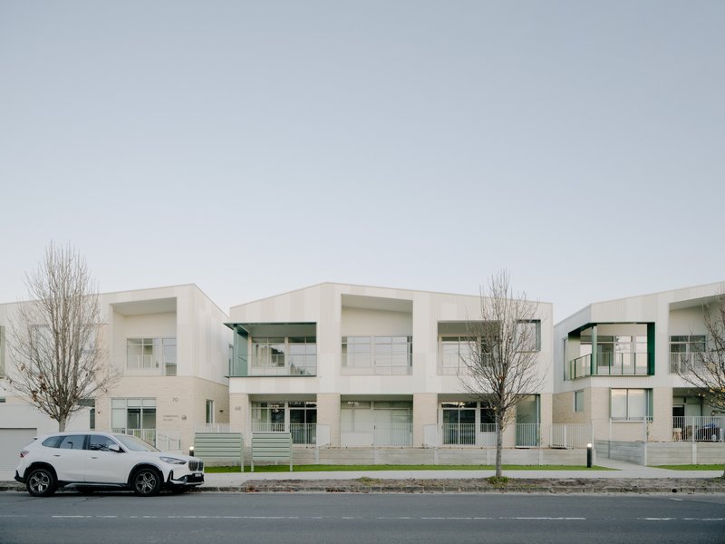 Street view of white residential facade with recessed balconies and young winter trees