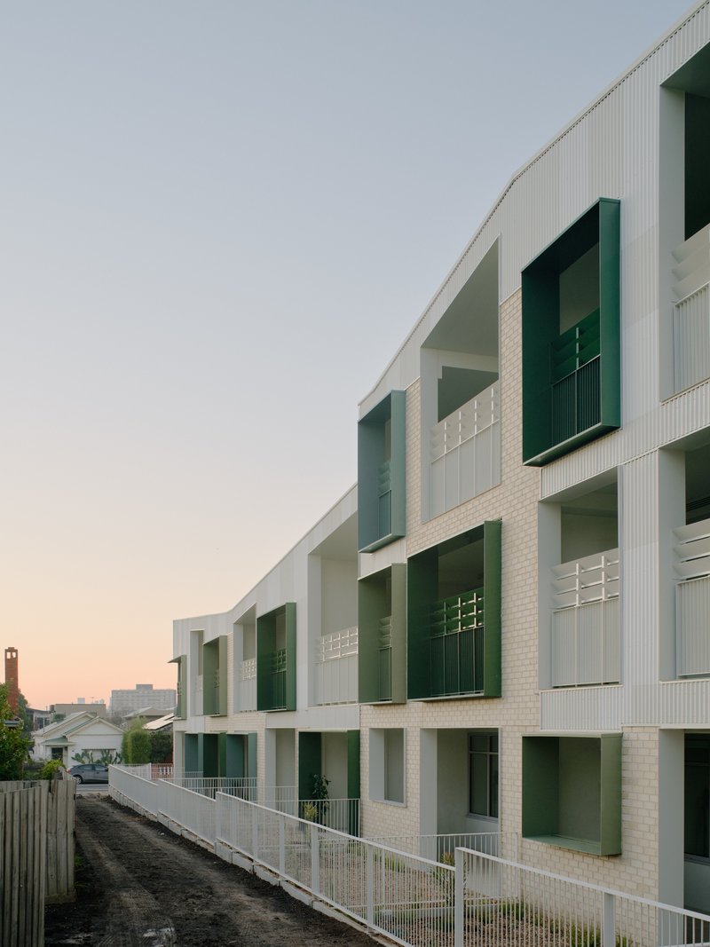 Perspective view of white brick facade with deep-set balconies at sunset