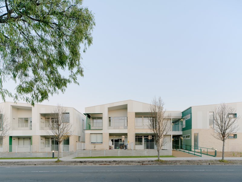 Street view of the two-story facade with white corrugated cladding, recessed balconies and bare winter trees