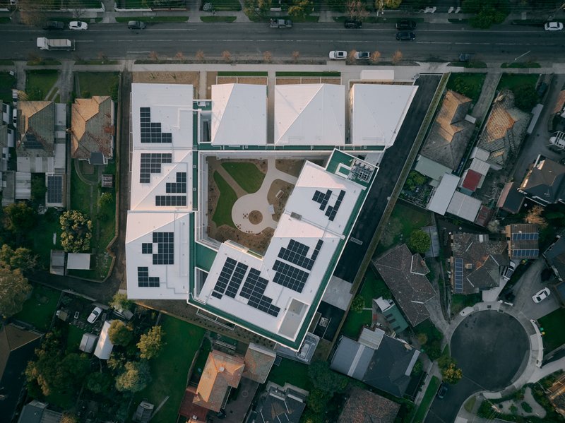 Aerial view of flat rooftops with solar panel arrays and shared courtyard gardens in a dense urban neighborhood