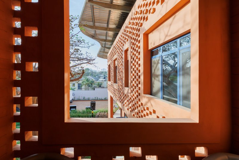 View through perforated brick wall opening to courtyard showing curved facade and metal canopy beyond