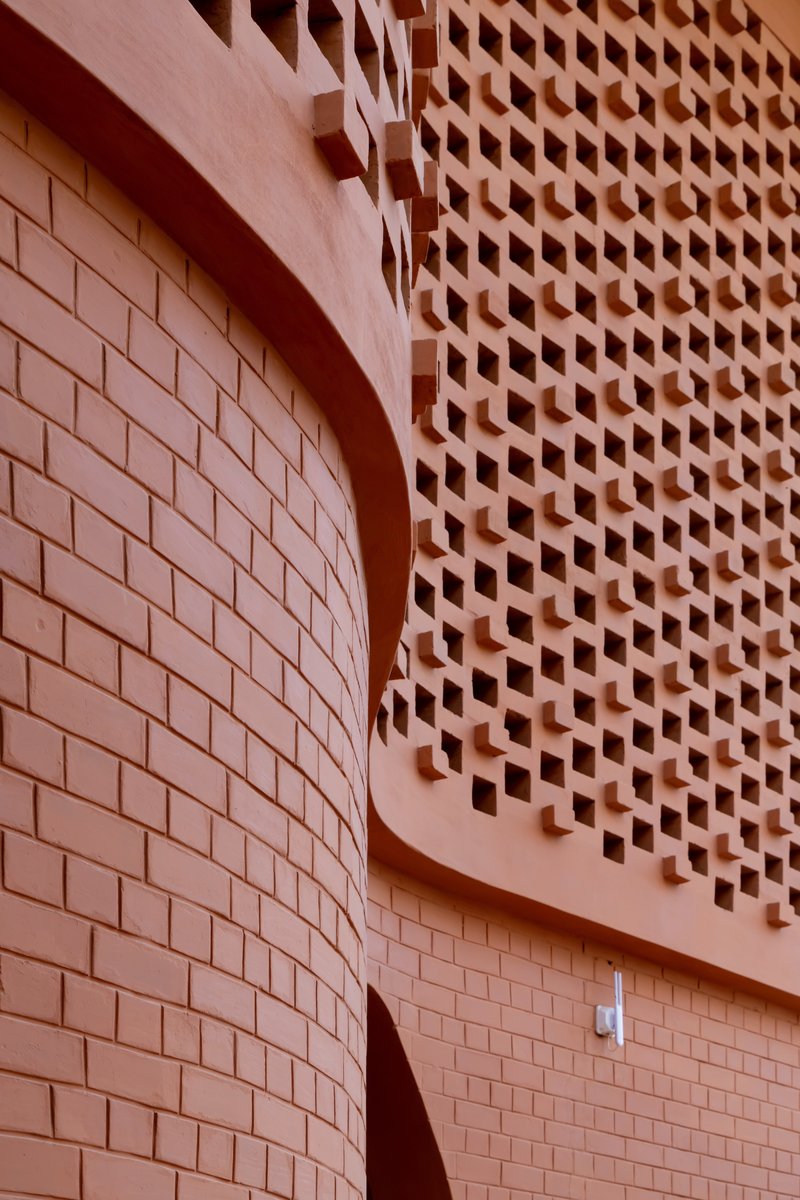 Close-up of curved terracotta block wall meeting perforated brick screen in afternoon shadow