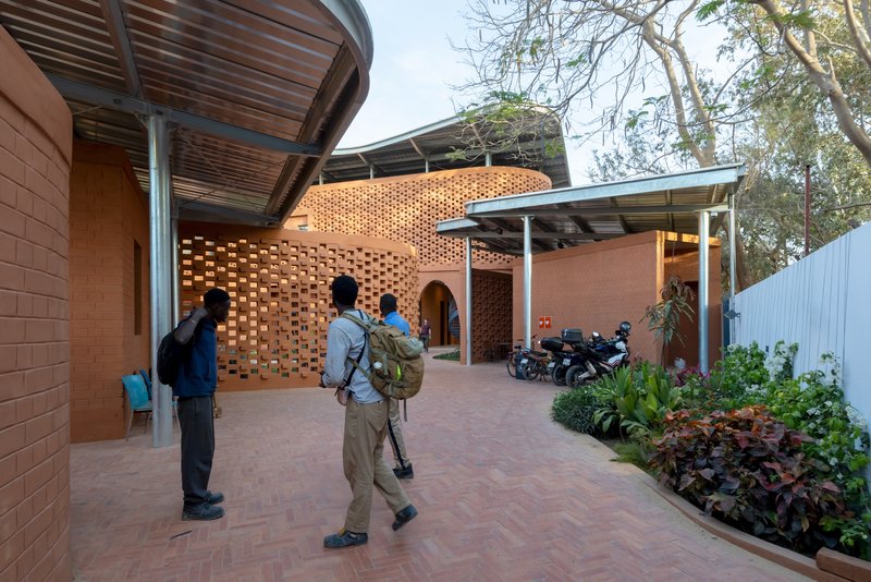 Courtyard entry with perforated brick walls and visitors walking on patterned pavers beside planted beds