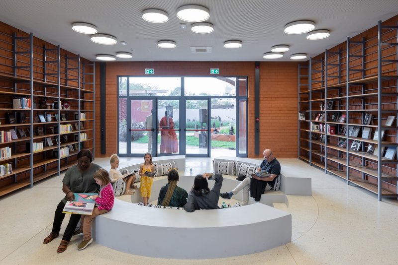 Reading room with circular seating platform, timber bookshelves, and visitors beneath clustered ceiling lights