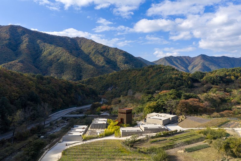 Aerial view of the compound nestled in a mountain valley with terraced gardens and a winding river below