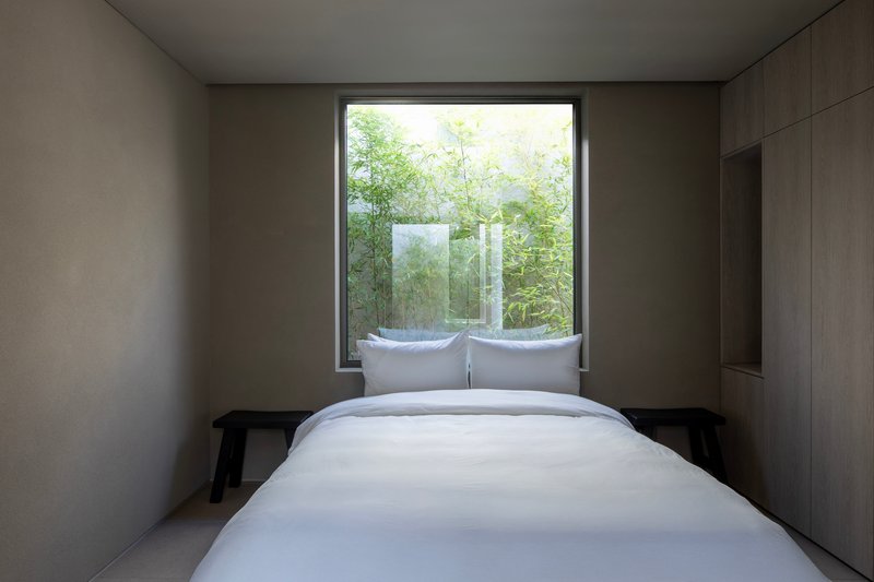 Bedroom with timber-lined walls and window framing a planted courtyard with translucent glass screen
