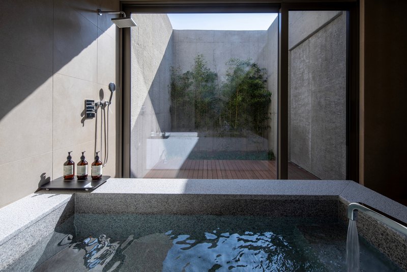 Sunken stone bathtub with rain shower facing a private courtyard with bamboo through floor-to-ceiling glass