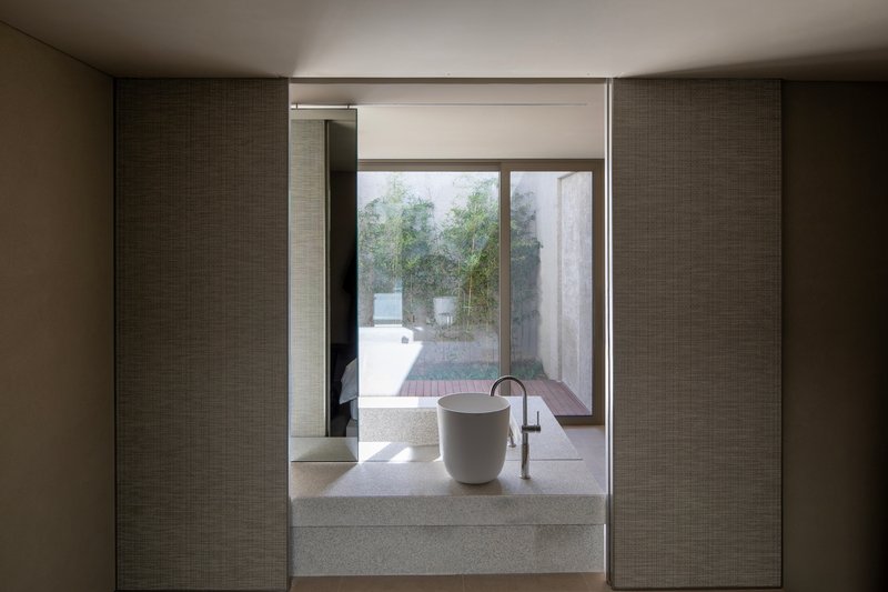 Terrazzo basin and freestanding tub framed by textured wall panels overlooking a courtyard in soft daylight