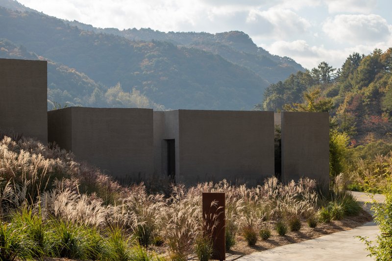 Concrete volumes with door openings set among native grasses with mountains and clouds in the background