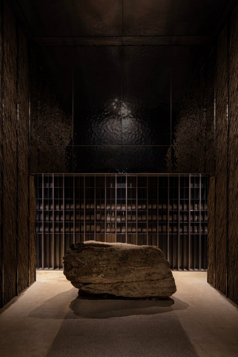 Entry hall with large stone boulder on plinth behind metal grille and dark wood paneling