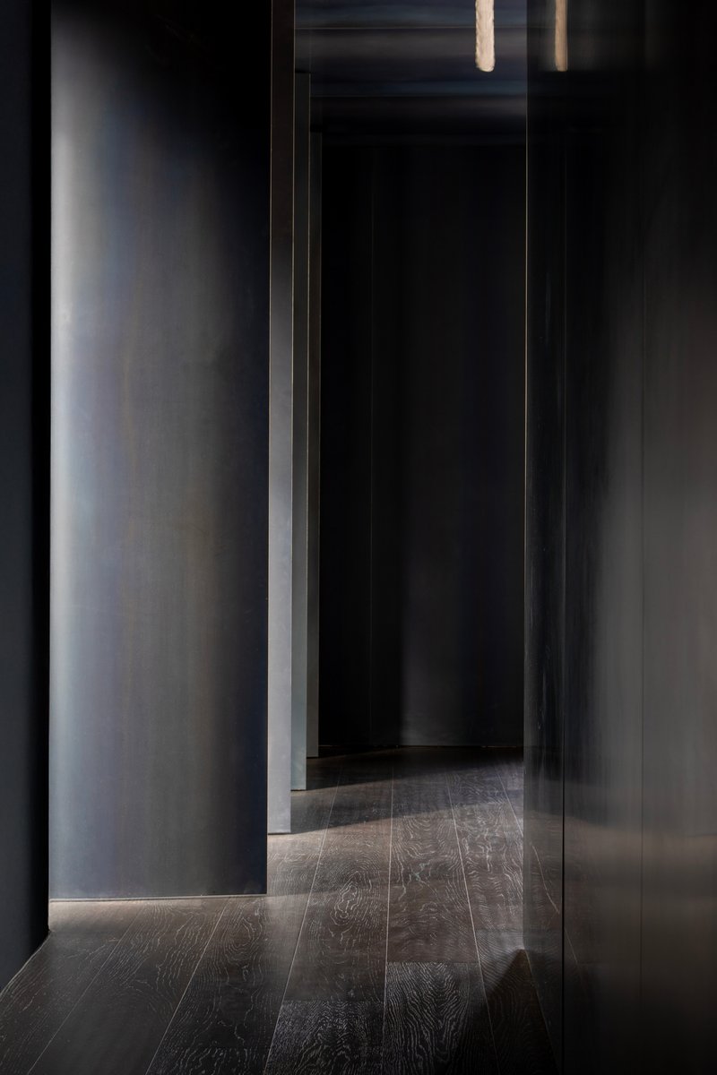 Narrow corridor with dark timber flooring and grey plastered walls lit by recessed strip lighting