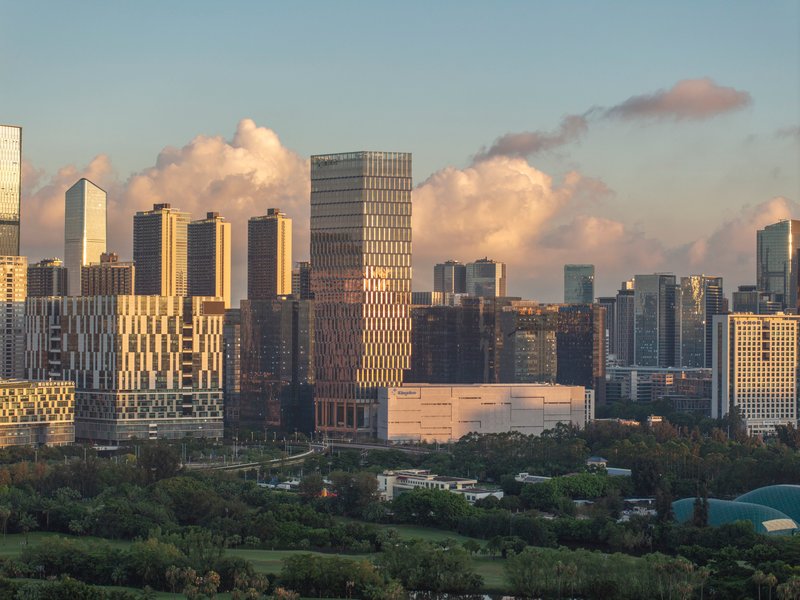 Tall tower with gridded facade rising above park landscape and skyline at golden hour