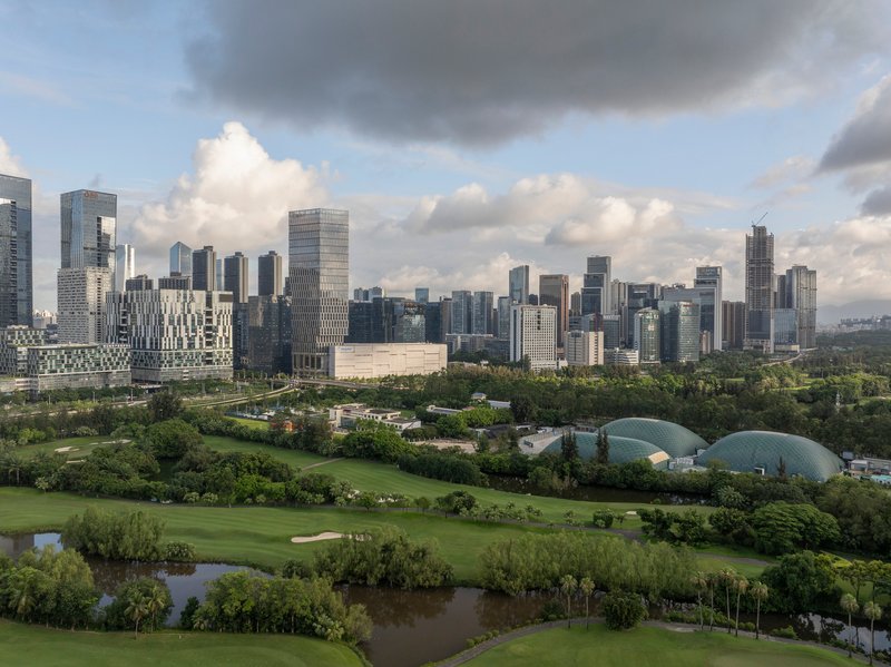 Skyline view showing tower and domed glass structures set within parkland under cloudy skies