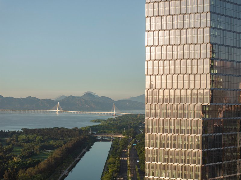 Close-up of gridded glass facade overlooking waterway with cable-stayed bridge and distant mountains