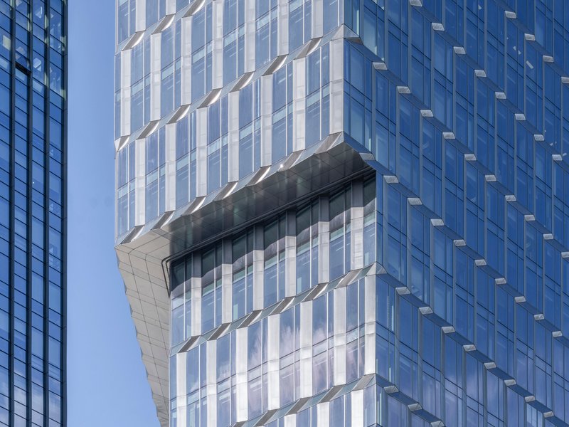 Close-up of the stepped glass tower facade with a protruding horizontal band under clear blue sky