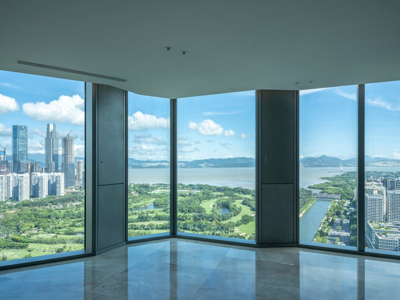 Corner window interior with floor-to-ceiling glass overlooking a golf course and waterfront on a cloudy day