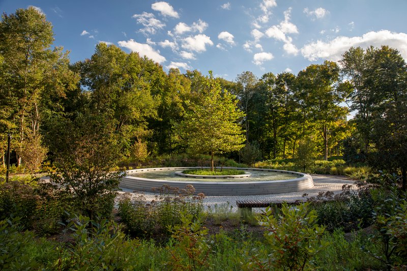 Long view of the circular memorial set within native plantings under a clear blue sky