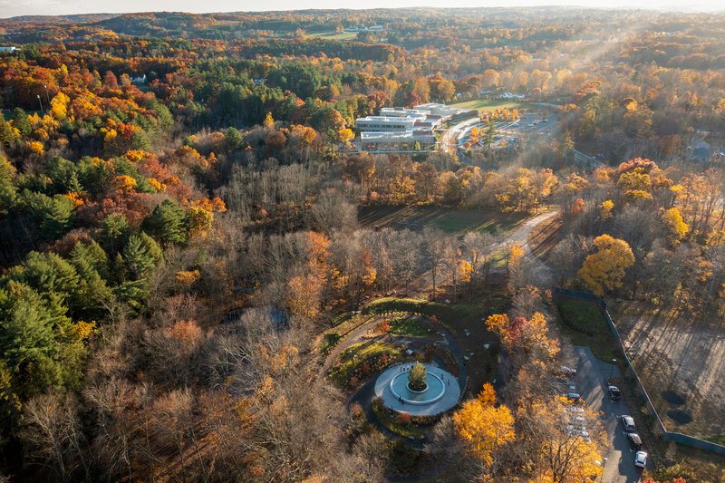 Long aerial view of the plaza in the forested valley with buildings visible in the distance