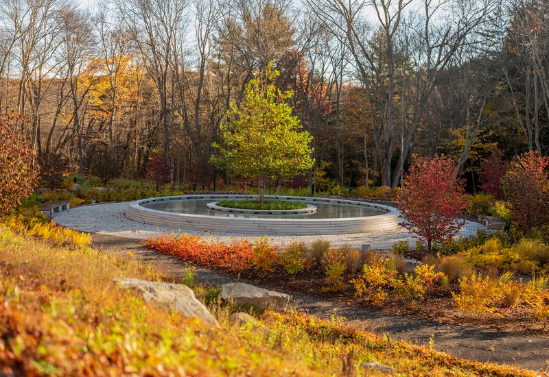 Circular memorial fountain with concentric granite rings and planted island surrounded by autumn foliage