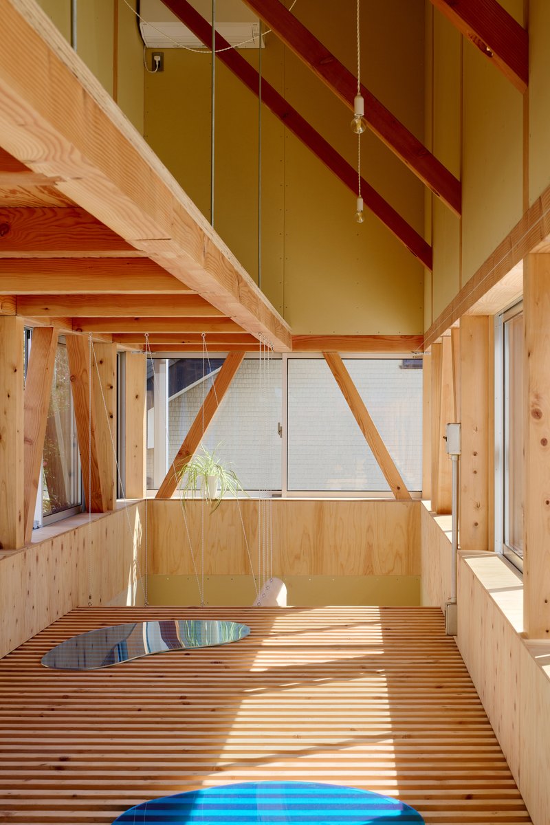 Interior view of slatted timber floor with diagonal structural beams crossing the vaulted ceiling in afternoon light