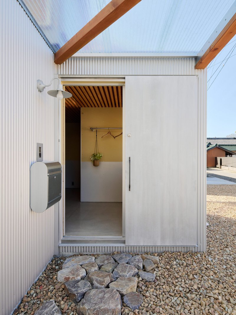 Entrance threshold with corrugated metal cladding and gravel ground beside a mailbox and stone border