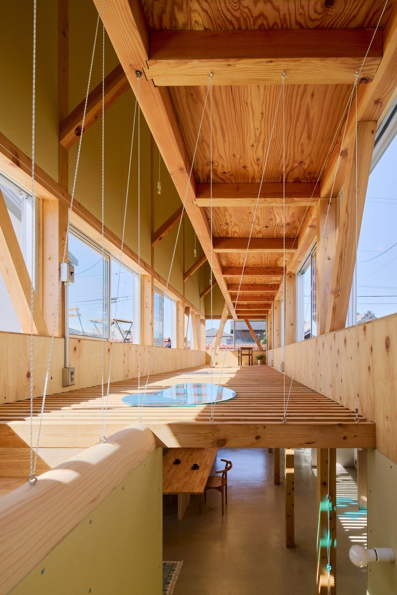 Suspended timber platform with circular opening overlooking a lower level in afternoon sunlight