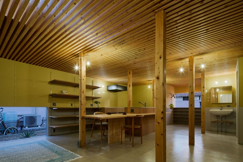 Interior view of timber-framed dining space with slatted ceiling and courtyard visible through low window at dusk