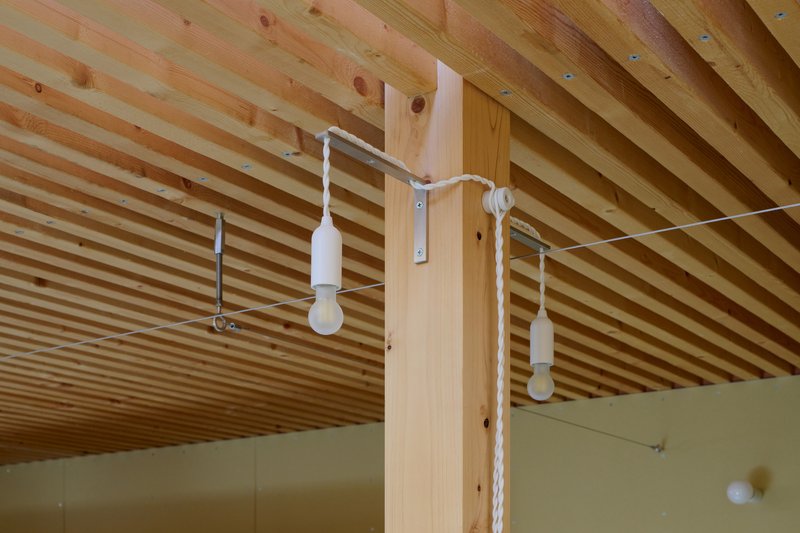White cord pendant lights suspended from timber post beneath exposed slatted ceiling joists