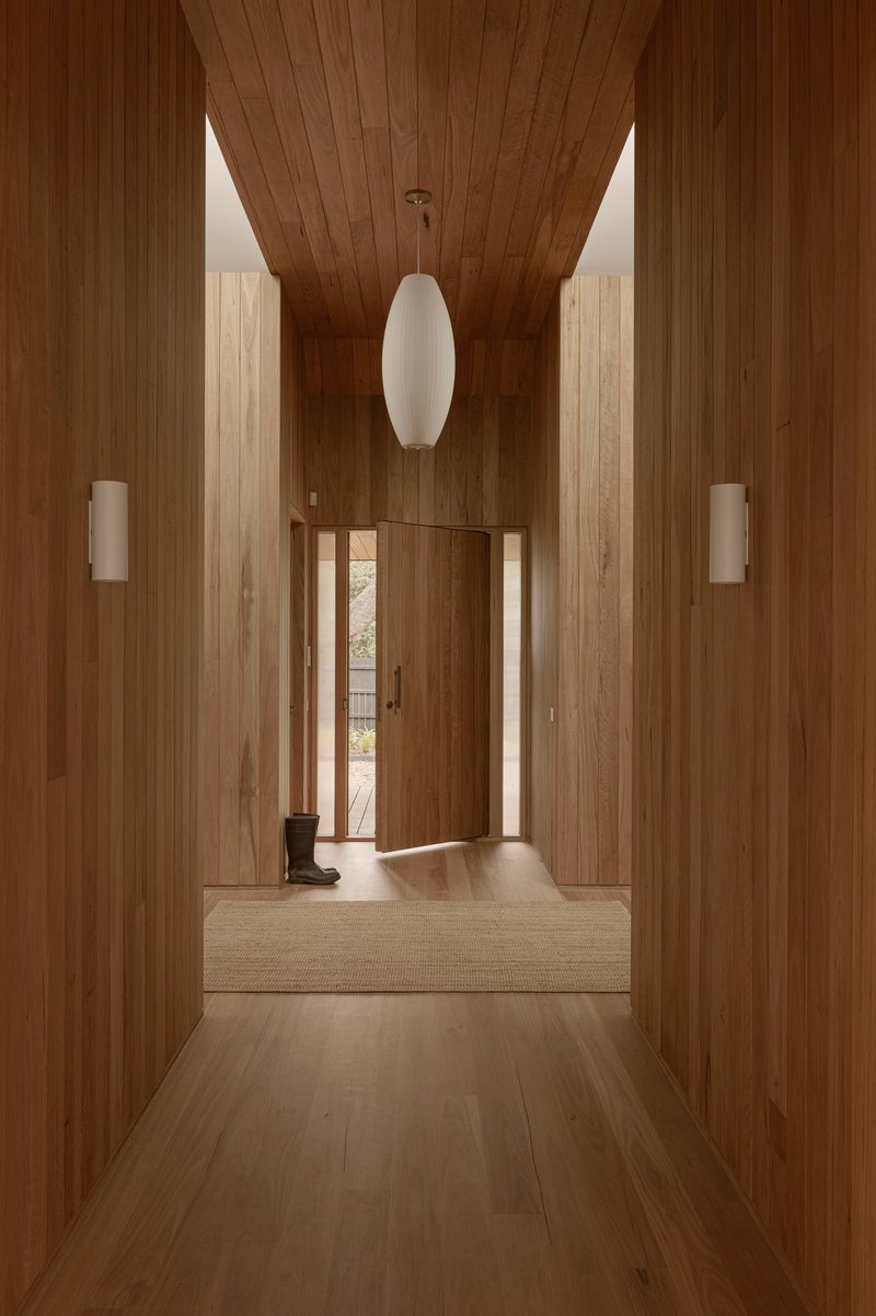 Timber-clad hallway with vaulted ceiling and white pendant light leading to an open entrance