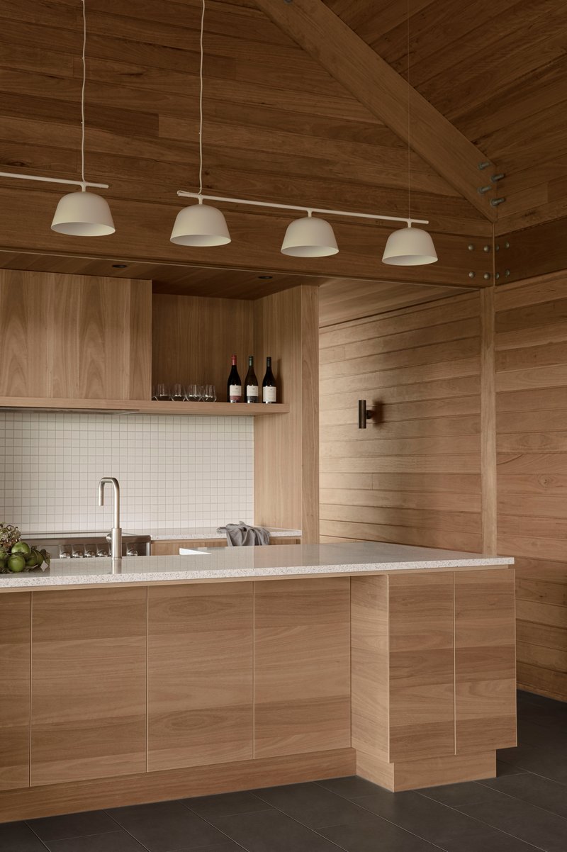 Kitchen island with white tile backsplash and timber cabinetry under a vaulted plank ceiling