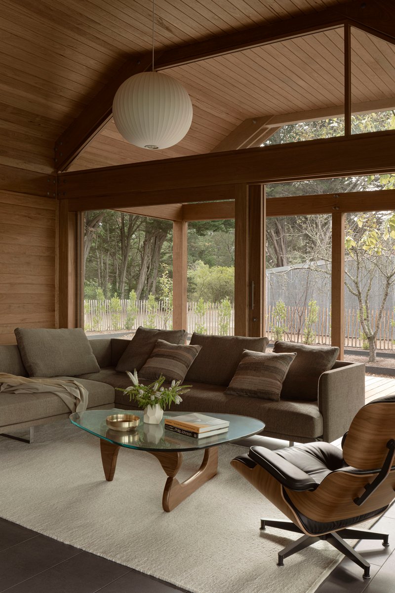 Living room with vaulted timber ceiling, clerestory windows, and views to surrounding trees through large glazing