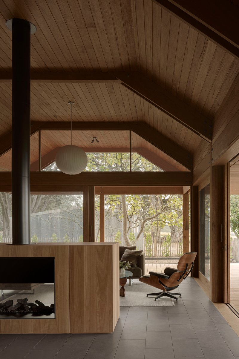 Interior living space with vaulted timber ceiling, pendant lamp, and glass walls framing garden views
