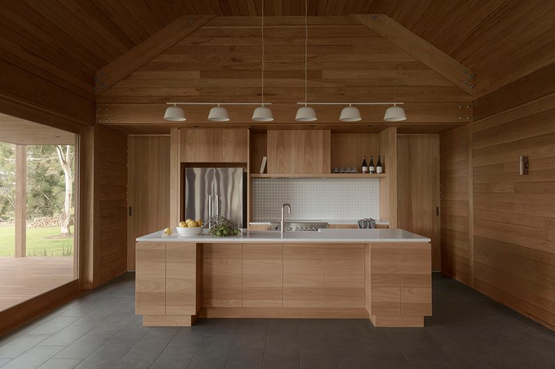 Timber kitchen island with white tile backsplash beneath a vaulted ceiling lined with six pendant lights